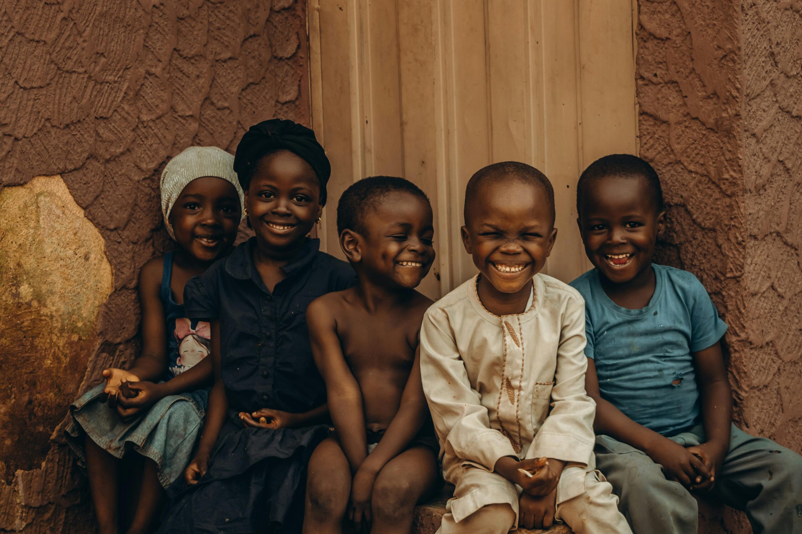 Five children smiling warmly in front of a textured wall, exuding joy and companionship.