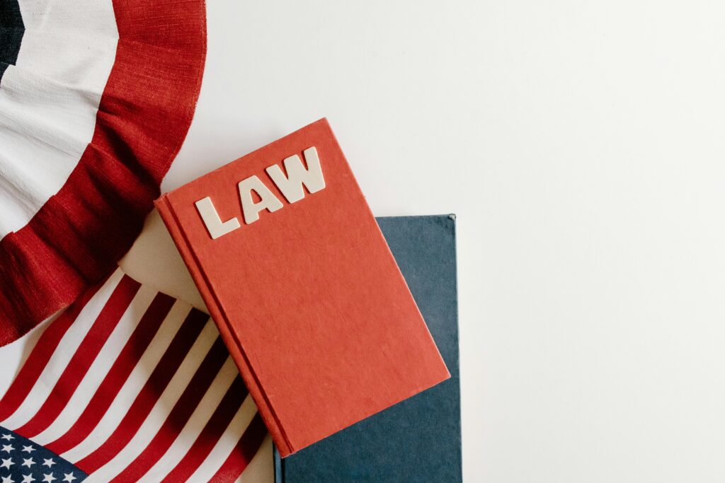 A flat lay of a red law book, American flag, and ribbon displaying patriotic themes.