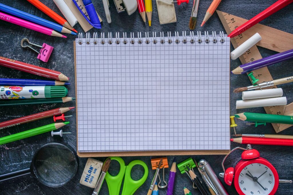 A vibrant flat lay of school supplies including a notebook, pens, pencils, and an alarm clock, ideal for educational themes.